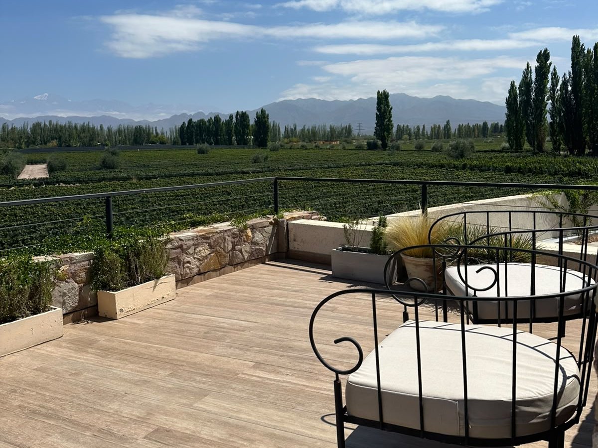 A terrace with two black iron chairs looking out over vineyards and the Andes under a blue sky